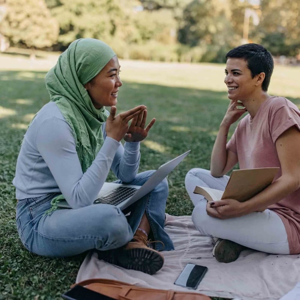 Two friends sitting on the grass talking